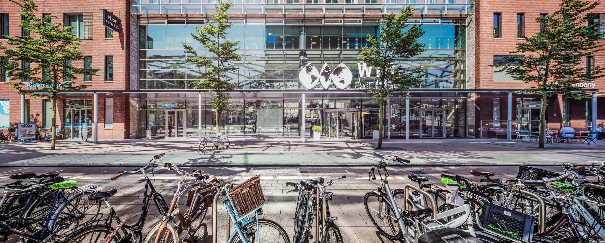 Ingang van het moderne WTC-gebouw aan de Prinses Beatrixlaan met fietsenrekken op de voorgrond.